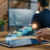 Une main utilise une tablette affichant des icônes holographiques de courriels et de bulles de chat en croissance.