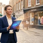 Une femme d'affaires utilisant une tablette numérique avec des effets lumineux dans une rue commerçante.