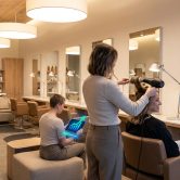 Une coiffeuse travaillant dans un salon moderne avec une collègue consultant des graphiques de croissance sur une tablette.